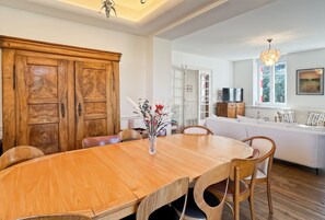 Un comedor con una mesa y sillas de madera, un jarrón con flores y un sofá blanco al fondo.