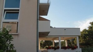 A modern two-story building with a balcony and a covered outdoor seating area. - Apartments Radmila (Sibenik)