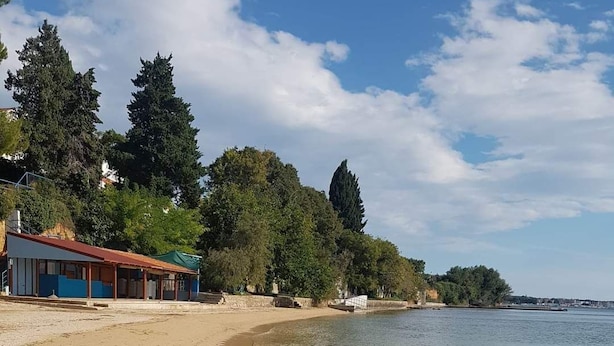 Ein Strand mit klarem Wasser, sandigem Ufer und einem Gebäude mit rotem Dach.