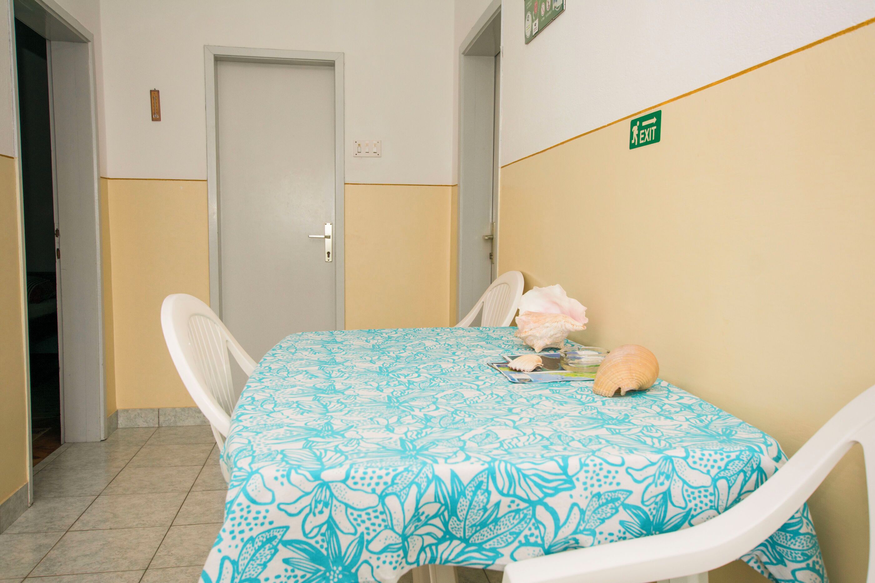 A hotel room with a bed, a table with a floral tablecloth, and a wall with an exit sign.