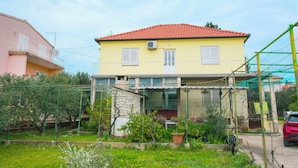 Ein zweigeschossiges Haus mit rotem Ziegeldach, einem Balkon und einem Garten mit Kübelpflanzen.
