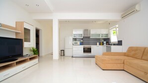 Un salon moderne avec un téléviseur à écran plat, un canapé beige et une cuisine en arrière-plan.