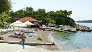 Une plage avec des parasols, des chaises longues et un bâtiment en pierre surmonté d’un toit rouge.