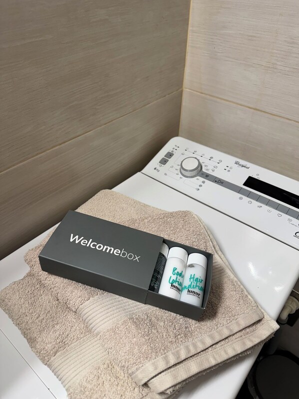 Une salle de bain avec une douche Whirlpool blanche, une serviette beige et une boîte d’accueil contenant une lotion pour le corps et un gel hydroalcoolique.