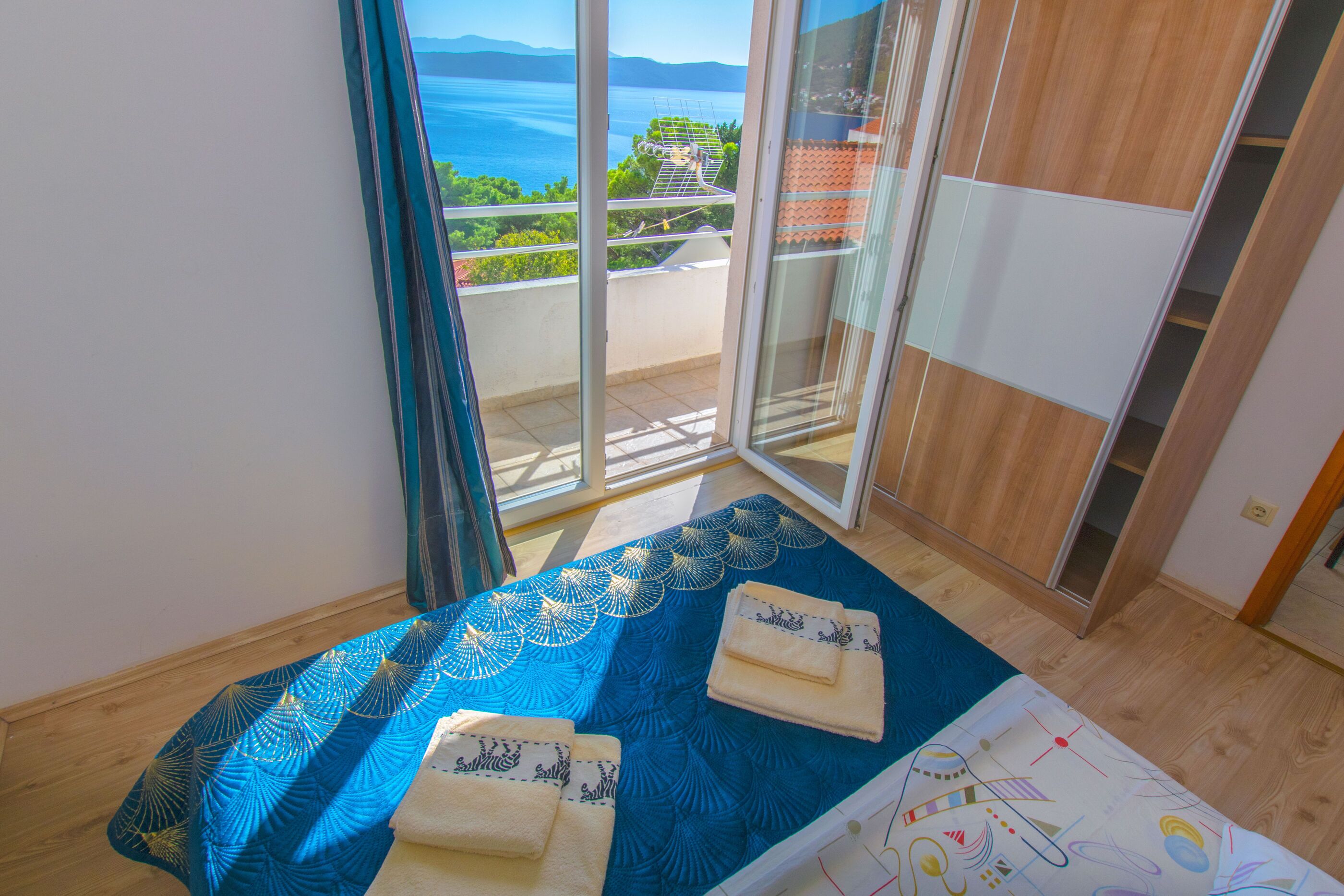 Un dormitorio con balcón, una cama con colcha azul estampada y dos toallas.