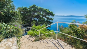 Una scala in pietra conduce a un punto panoramico con vista sul mare e un albero grande.