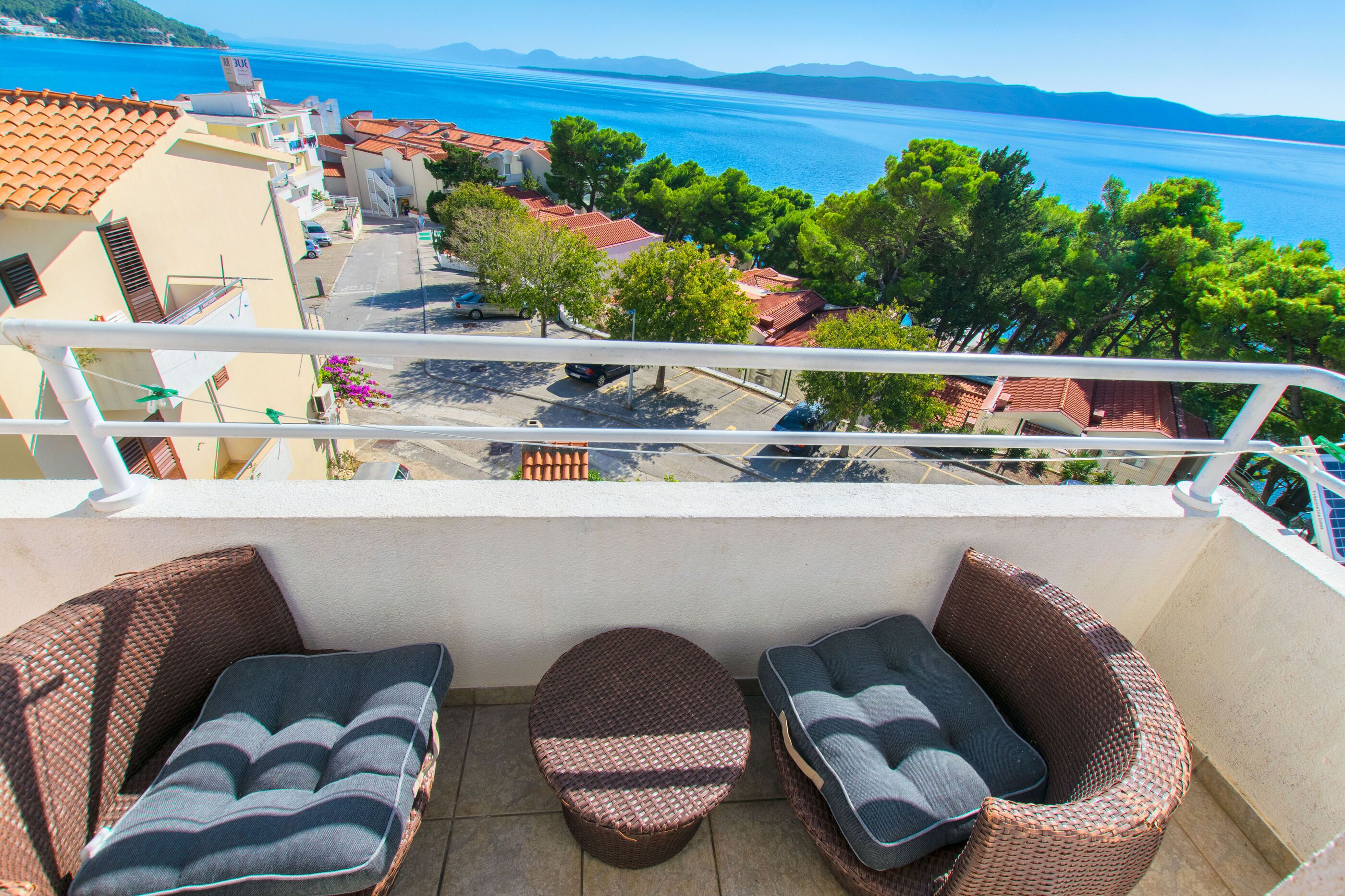 Un balcon doté de meubles en osier et offrant une vue sur la mer et les bâtiments.
