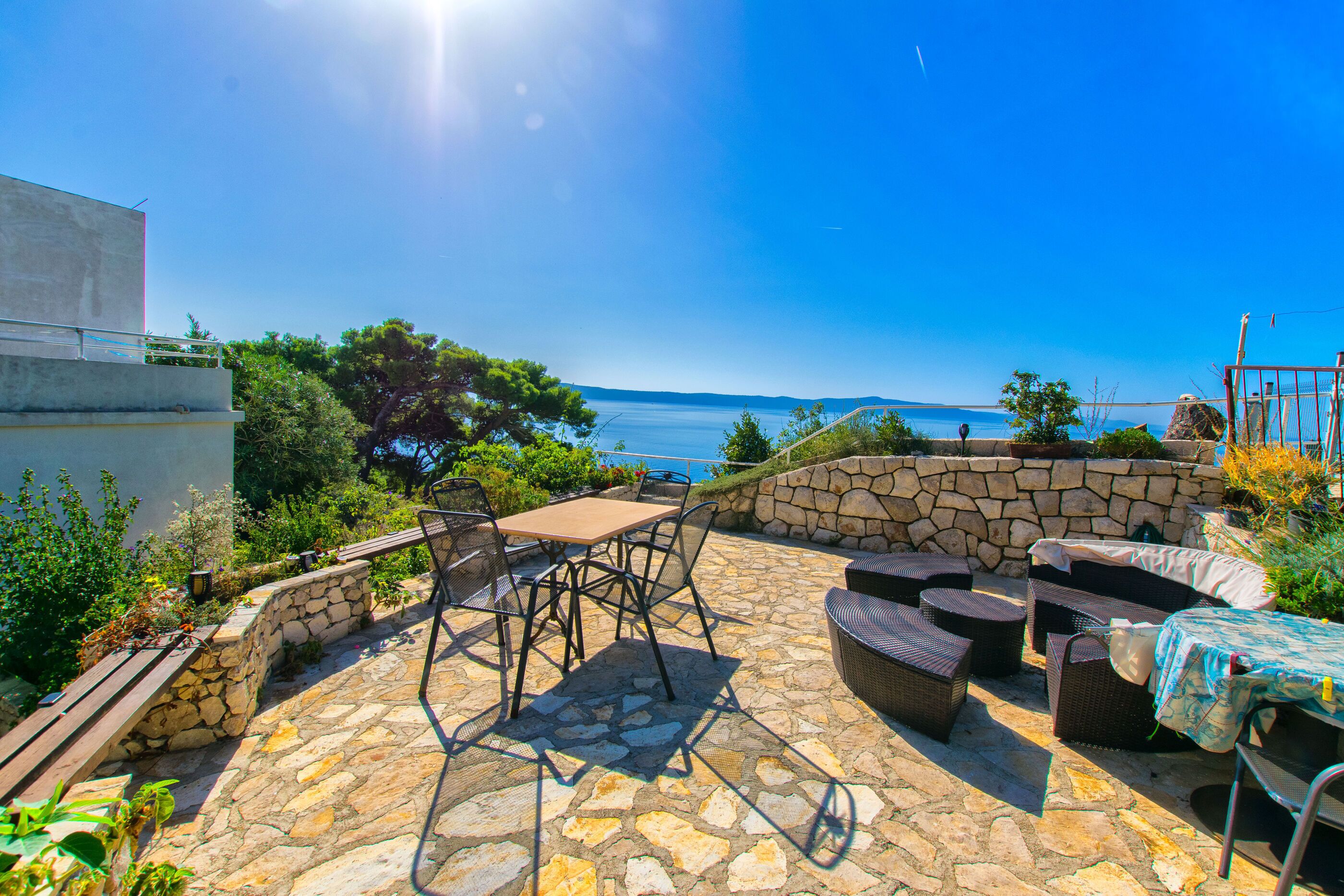 Une terrasse extérieure avec un sol en pierre, une table et des meubles en osier, donnant sur une étendue d’eau.