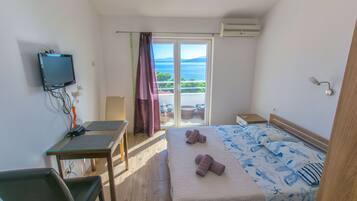 Een slaapkamer met een bed, een bureau, een stoel, een televisie en een balkon met uitzicht op zee.