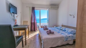 Una camera da letto con un letto, una scrivania, una sedia, un televisore e vista mare tramite una porta scorrevole.