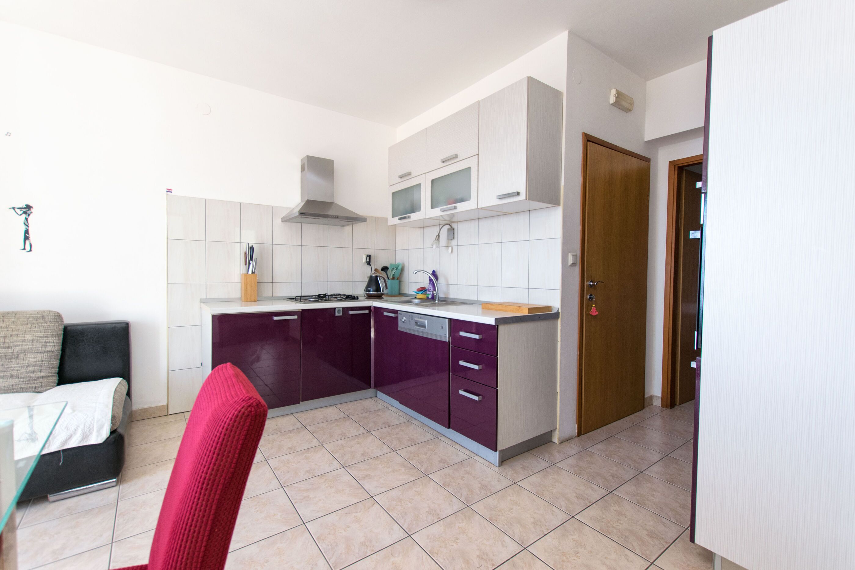 A compact kitchen with white and purple cabinets, a microwave, and a stove. There is a red chair and a small dining table.