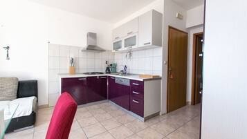 A compact kitchen with white and purple cabinets, a microwave, and a stove. There is a red chair and a small dining table.