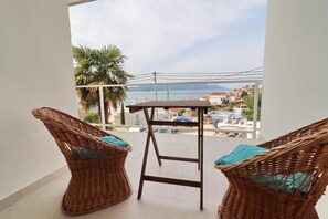 A balcony with wicker chairs and a table, overlooking a coastal town and the sea. - House Rosemary (Slivno)