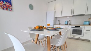 A modern kitchen with white cabinets, a white dining table with four chairs, and a breakfast setting with fruits and orange juice. - House Rosemary (Slivno)