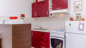 Une cuisine de taille réduite avec des meubles rouges, une cuisinière blanche et un évier.