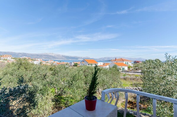 A terrace with a potted plant, overlooking a coastal village with houses and a clear sky.