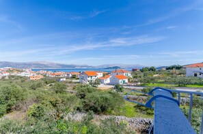 A coastal village with white buildings and red roofs, surrounded by greenery and mountains in the background.