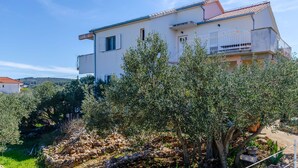 Une maison à deux étages avec un balcon, entourée d’oliviers et d’un mur de pierre.