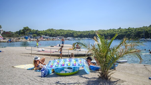 A beach with a pool, people sunbathing, and a large inflatable pool with colorful cups. - Apartments Maris (Tribunj)