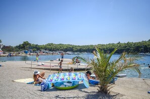 A beach with a pool, people sunbathing, and a large inflatable pool with colorful cups. - Apartments Maris (Tribunj)