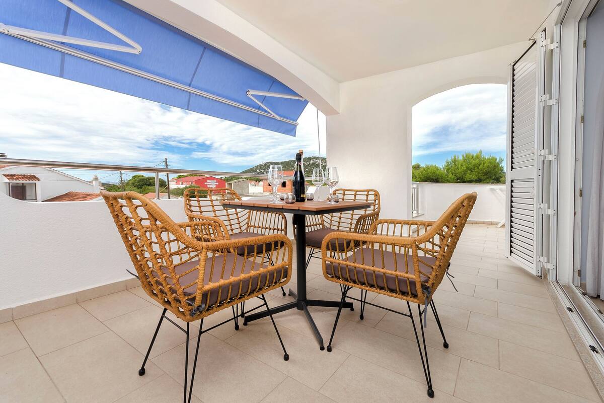 A balcony with a table and four wicker chairs, a bottle of champagne, and two glasses.