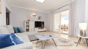 A modern living room with a grey sofa, a coffee table, a TV, and a balcony with outdoor furniture. - Apartments Maris (Tribunj)