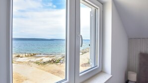 A room with a large window overlooking a beach and the sea. - House Sea Stone (Pasman)