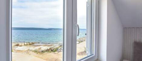 A room with a large window overlooking a beach and the sea.