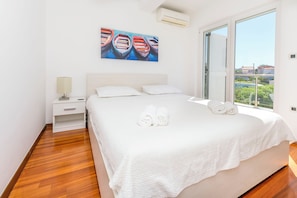 Camera da letto con un letto grande, un comodino, un quadro con barche e vista su del verde attraverso una finestra.