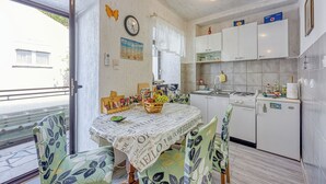 Una cucina compatta con zona pranzo, che include un tavolo con tovaglia a motivi floreali, sedie, un cesto di frutta e una sveglia appesa al muro.
