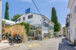 Eine schmale Straße mit einem Gebäude, das einen Glasvordereingang, abgestellte Roller und hohe Bäume zeigt.