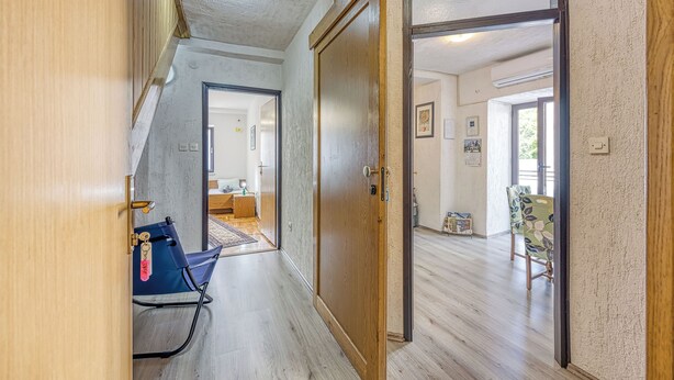 A hallway with a wooden door leading to a room with a bed and a window. - Apartment Selce (Crikvenica)