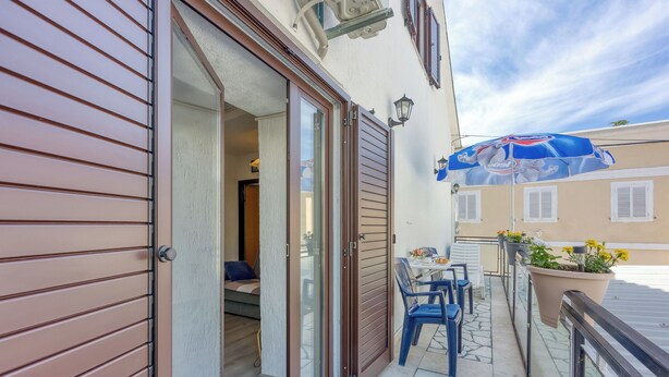 Un balcone con tavolo e sedie, una porta scorrevole in vetro e un ombrellone.