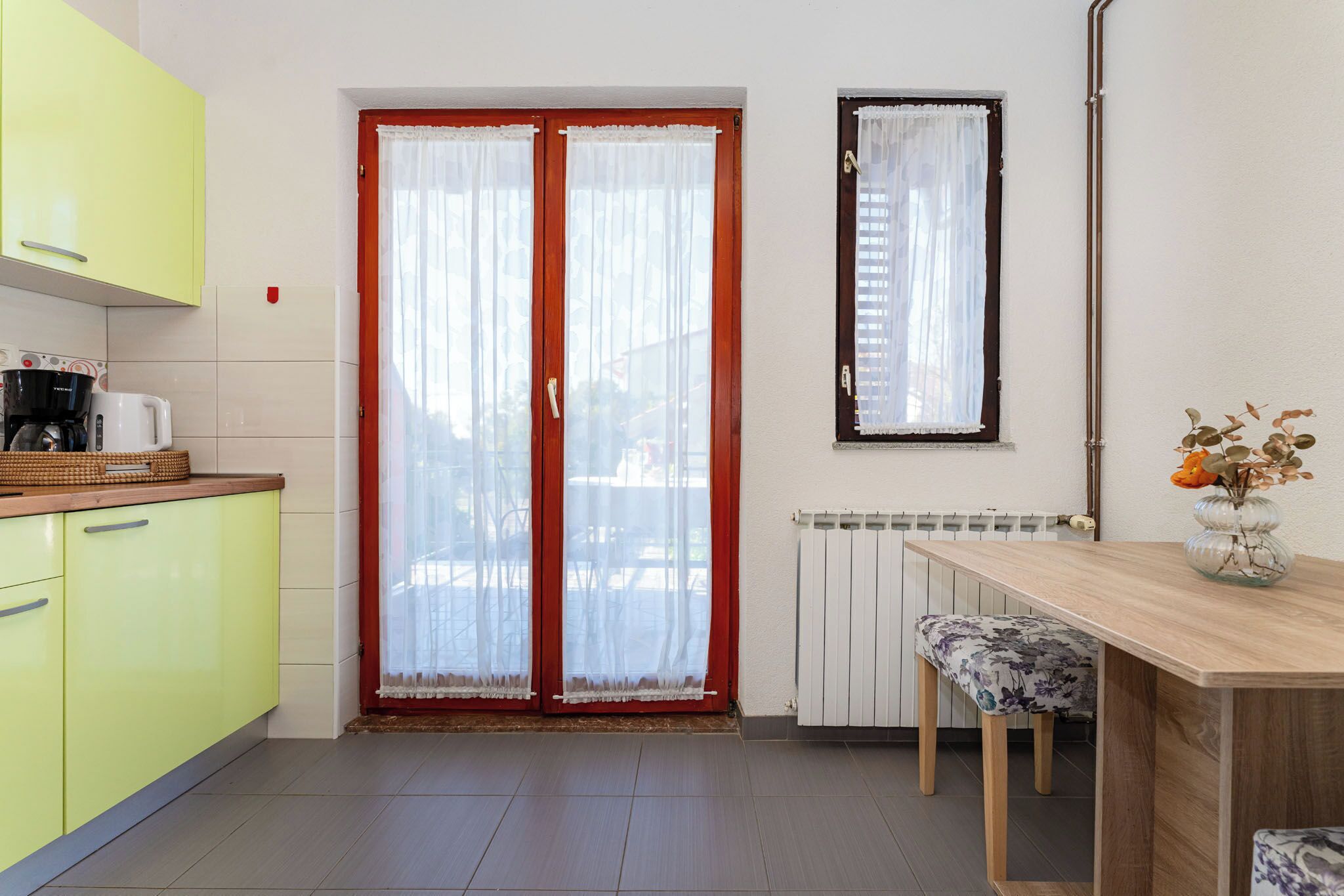 A kitchen with yellow cabinets, a wooden table, and a window with red curtains.