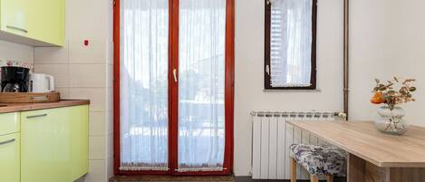 A kitchen with yellow cabinets, a wooden table, and a window with red curtains.
