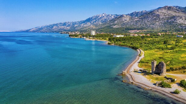 A coastal town with clear blue waters, a mountain range, and a historic stone structure. - Apartments and Room Adriana (Starigrad)