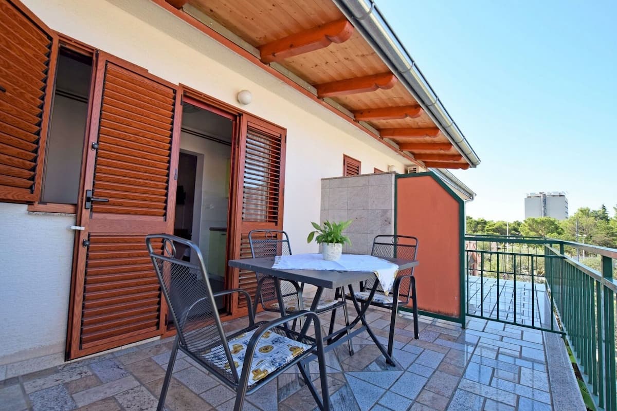 An outdoor patio with a table and chairs, a potted plant, and wooden shutters on the building.