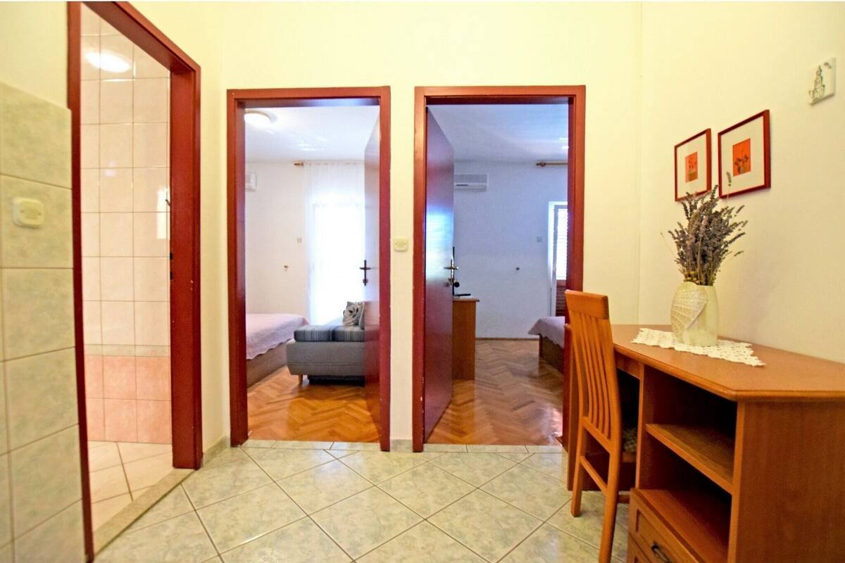 A hallway with a wooden floor, a dining area with a table and chairs, and a sofa in the background.