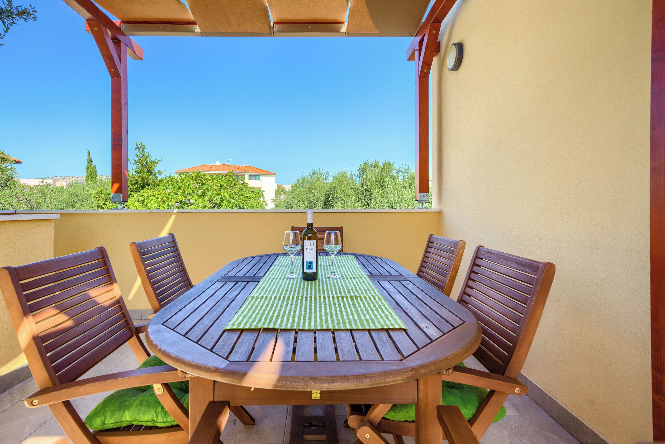 A round wooden table with four chairs, a green table mat, and a bottle of wine on the table.