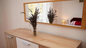 A wooden dresser with a mirror above it, a vase with dried plants, and a bed with a red and white striped pillow in the reflection. - Apartment Branka (Vodice)