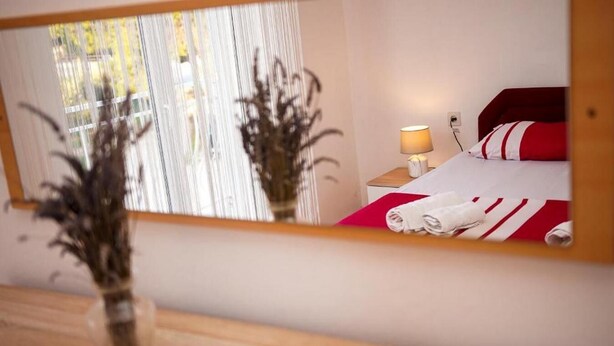 A hotel room with a bed, a nightstand, a lamp, and a mirror reflecting the room. - Apartment Branka (Vodice)