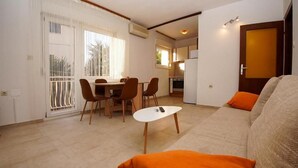 A living room with a sofa, orange cushions, a dining table with chairs, and a kitchen area in the background. - Apartment Branka (Vodice)