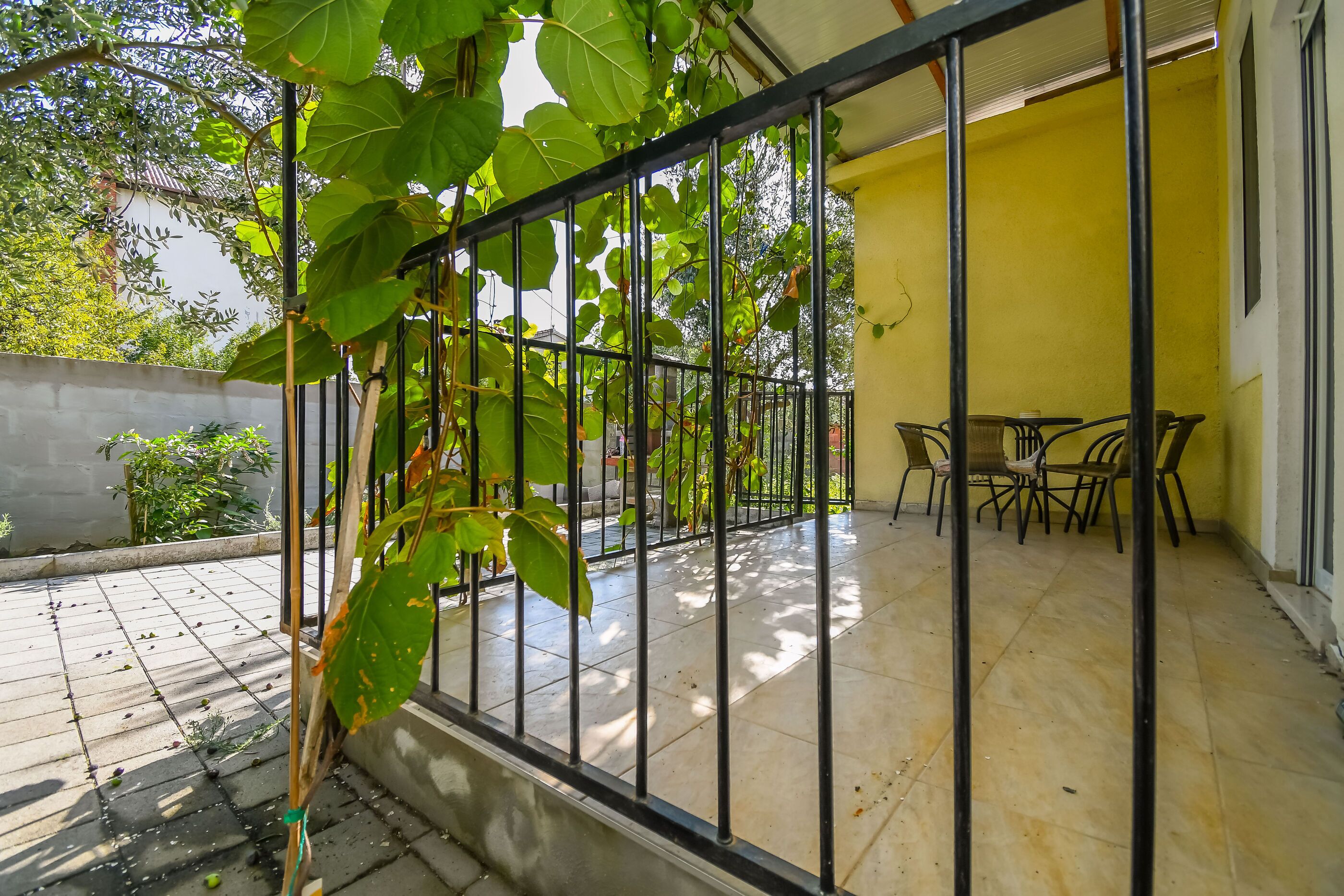 A covered patio with a tiled floor, a metal railing, and a table with chairs.