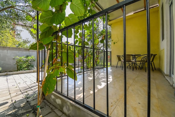 Um alpendre coberto com chão de azulejos, guarda-corpo de metal e uma mesa com cadeiras.