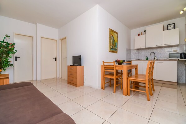 Um espaço compacto com cozinha compacta, área de jantar com mesa e cadeiras de madeira, TV e uma planta.