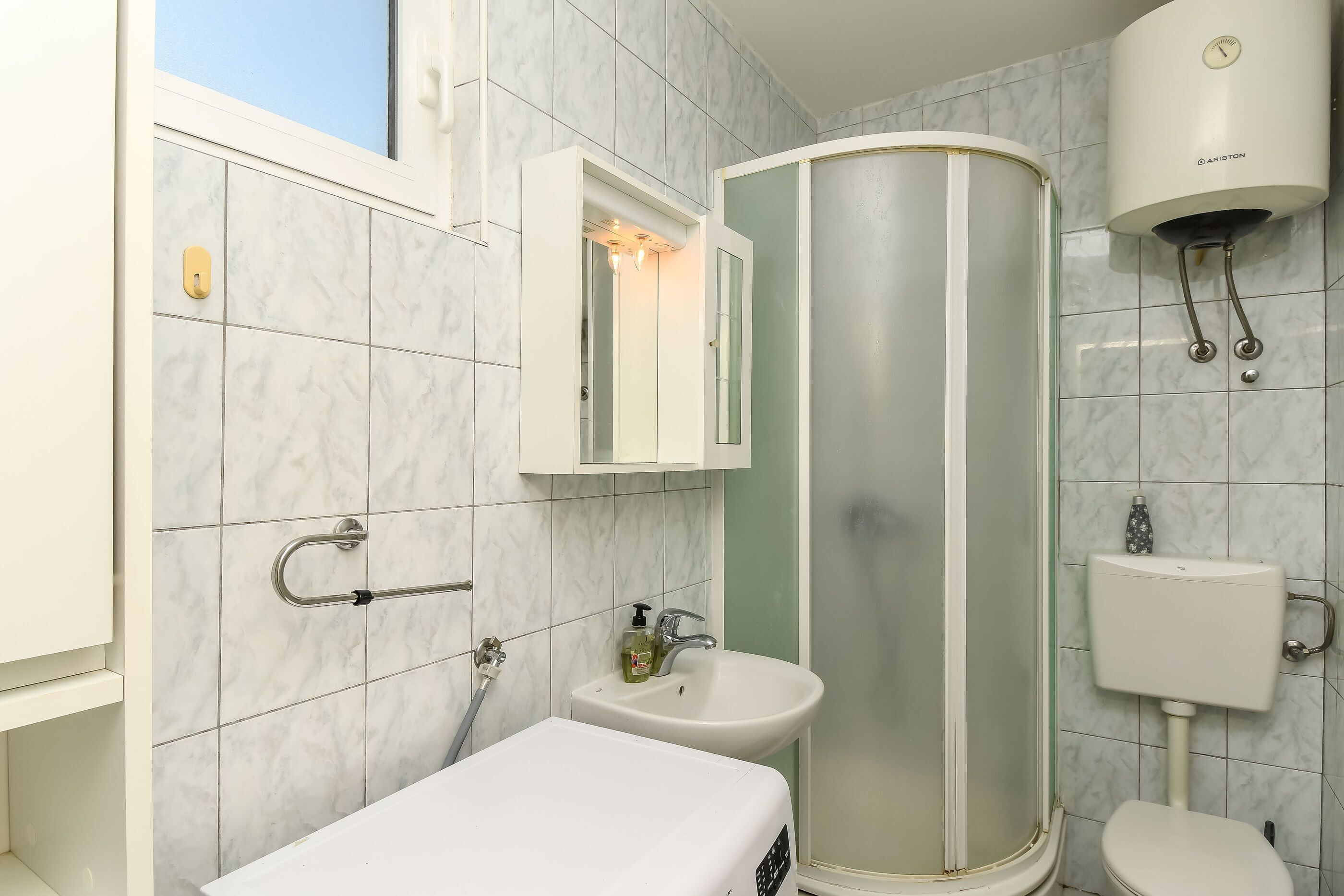 A bathroom with a shower, sink, and toilet, featuring marble tiles and a white vanity.
