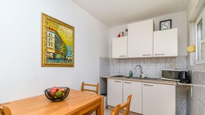Una cocina con alacenas blancas, microondas y pileta. Hay un cuadro en la pared y un frutero sobre la mesa.