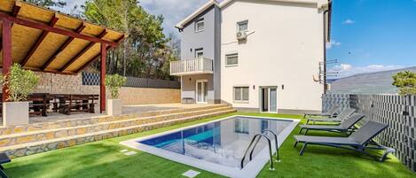 A modern building with a pool, outdoor seating, and a view of the landscape.