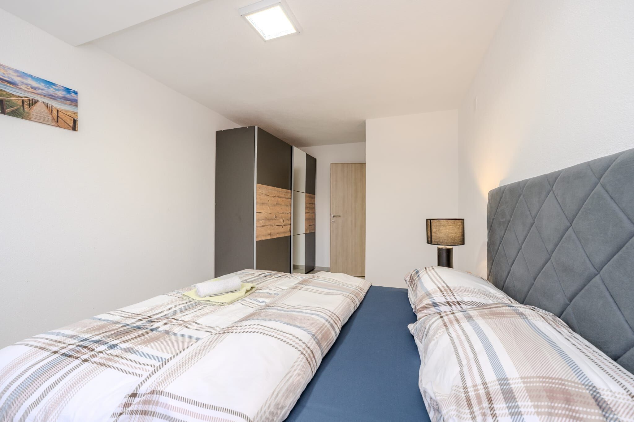 A bedroom with two beds, a wardrobe, a desk, and a painting on the wall.