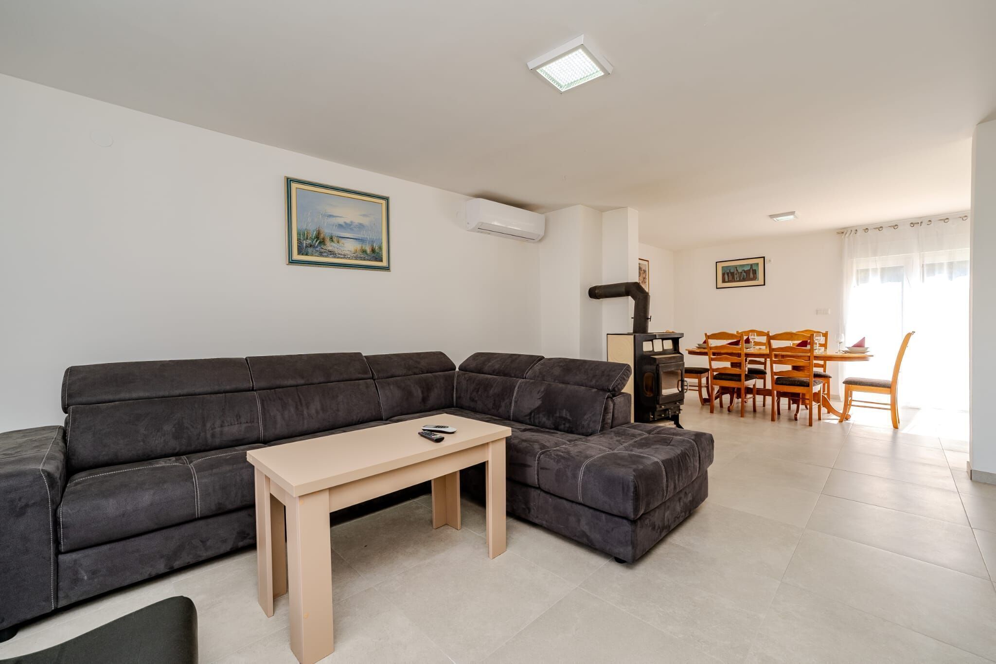 A modern living room with a sectional sofa, a wooden coffee table, and a dining area with wooden chairs and a table.